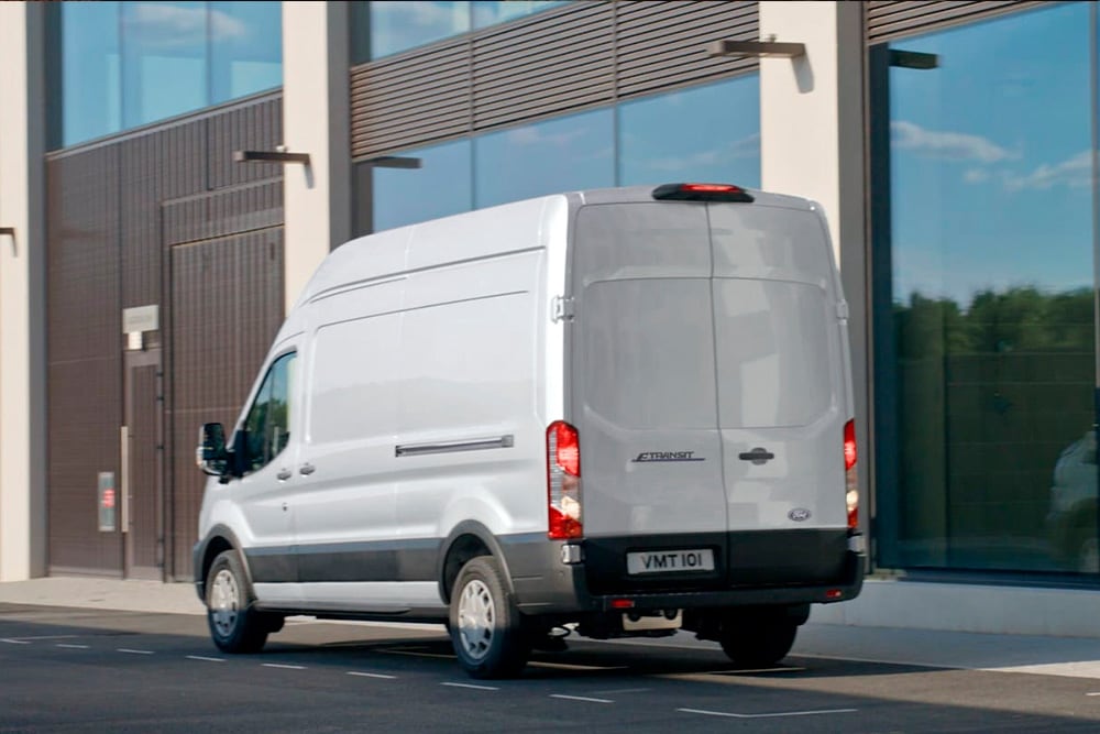 Achterzijde van een zilverkleurige  Ford Transit bestelwagen in een stadsstraat. 