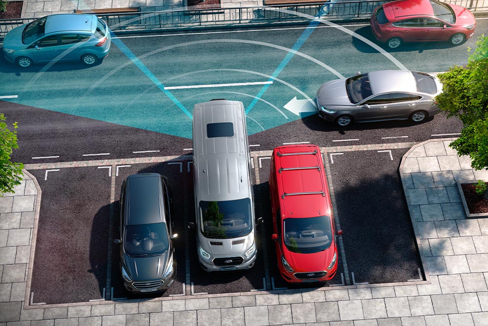 Zilverkleurige Ford Transit bestelwagen rijdt achteruit, met blauwe lijnen die het gebruik van de achterste parkeersensoren weergeven. 