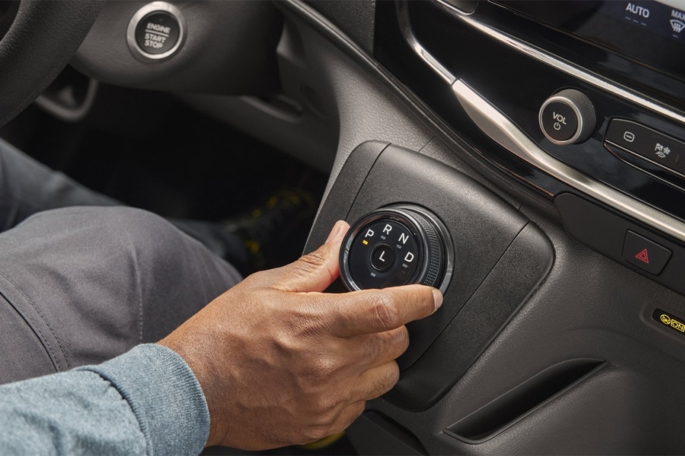 Een hand draait aan de schakelknop in de middenconsole van de  Ford Transit bestelwagen. 
