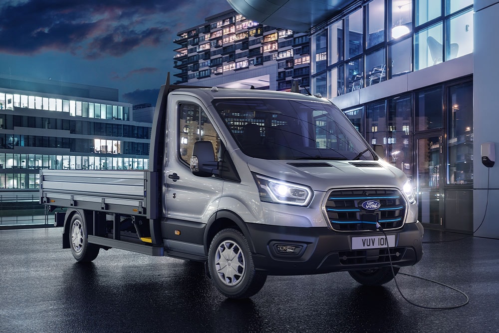 Zilverkleurige Ford E-Transit Chassis Cab  geparkeerd voor een modern gebouw in het donker.