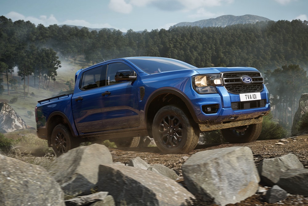 Een blauwe Ford Ranger pick-up rijdt over een onverharde weg door een bos en laat een spoor van stof achter.