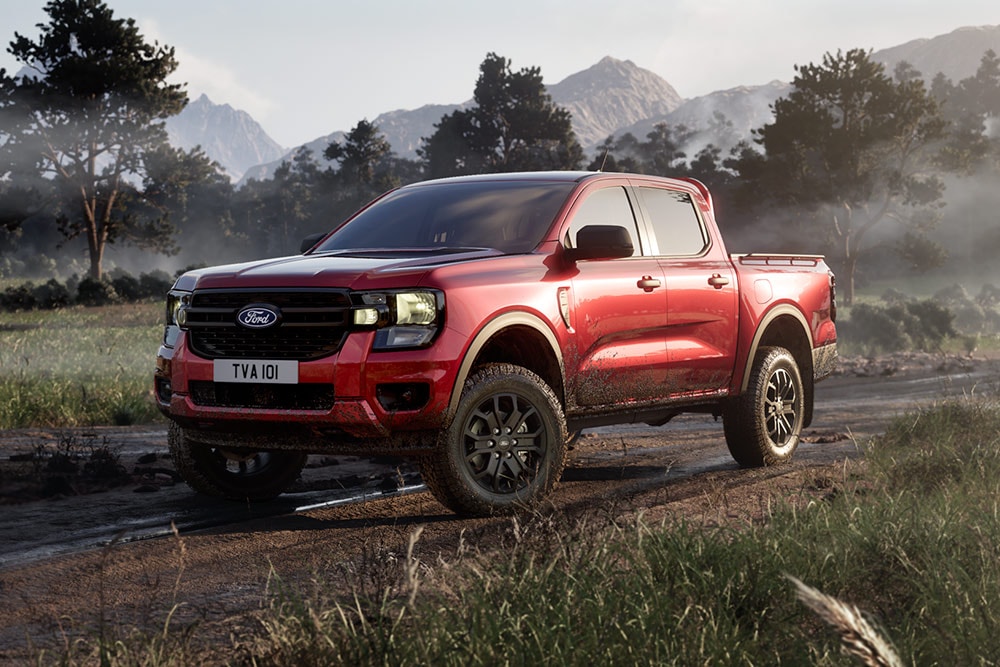 Een rode Ford Ranger Raptor rijdt op een onverharde weg door een schilderachtig landschap.