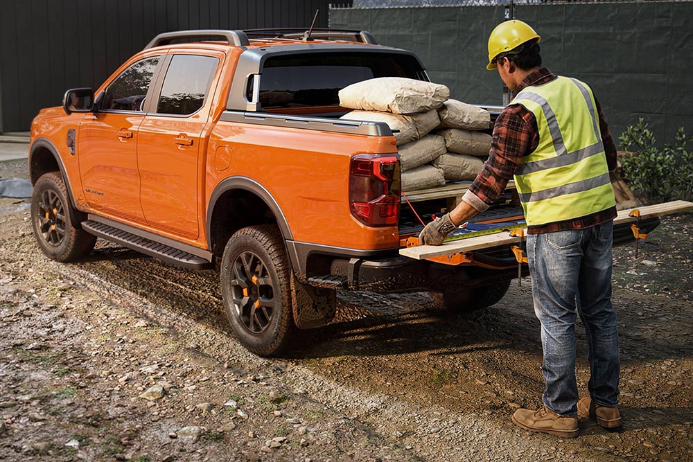 Een bouwvakker laadt materiaal op de laadbak van een oranje Ford Ranger.
