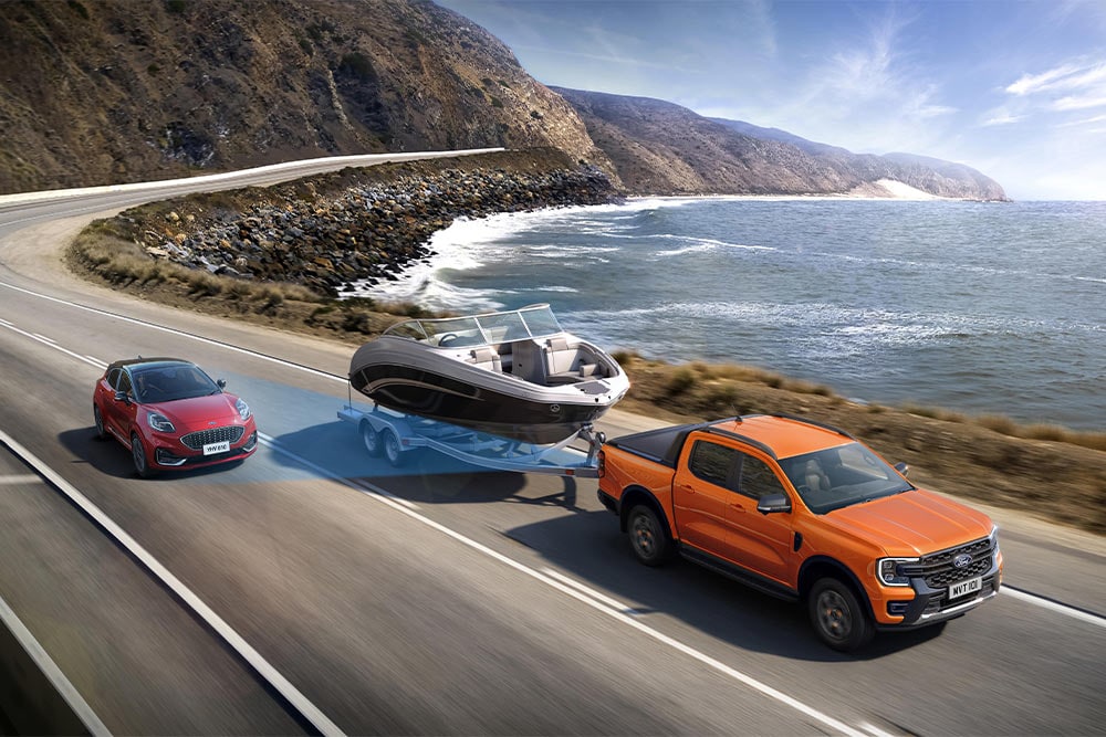 Een oranje Ford Ranger sleept een boot langs een kustweg en toont zijn trekvermogen.