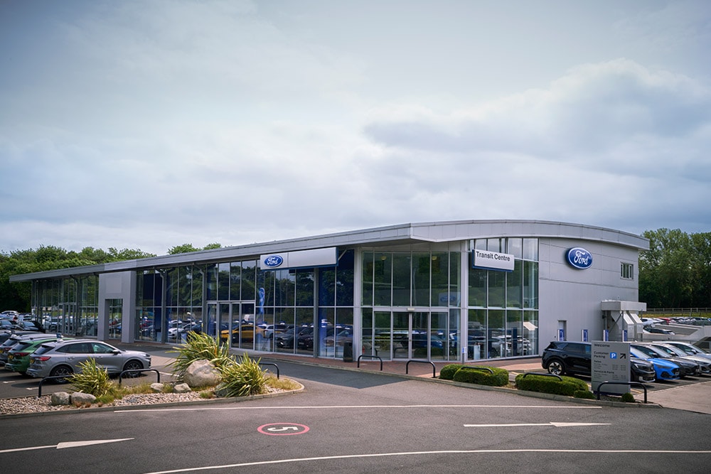 Buitenaanzicht van een modern gebouw van een Ford-verdeler met verschillende Ford-voertuigen die buiten geparkeerd staan.