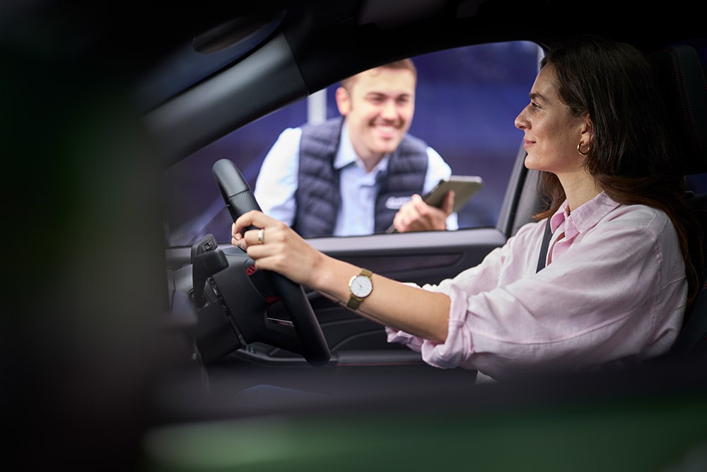 Een persoon op de bestuurdersstoel van een Ford-auto, kijkend naar een technicus die buiten een tablet vasthoudt.