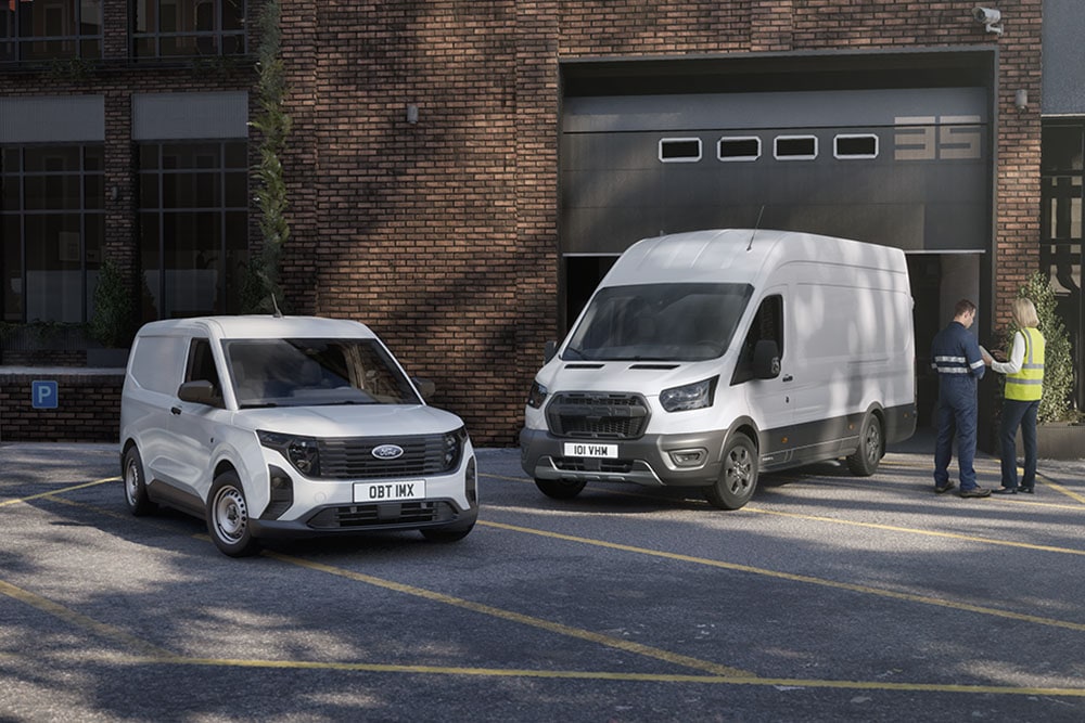 Twee witte Ford-bestelwagens geparkeerd voor een modern gebouw, twee mensen praten met elkaar naast de voertuigen.