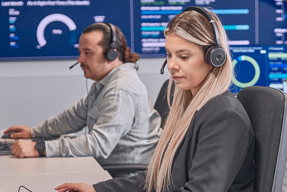  Twee mensen met headsets werken aan computers in een moderne controlekamer.