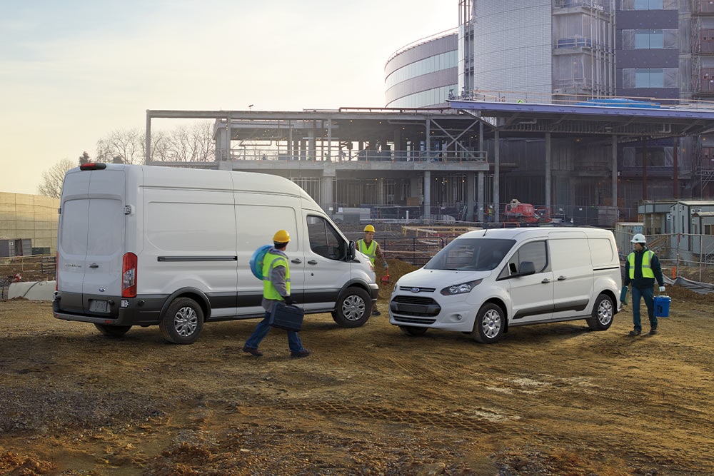 Twee witte Ford bestelwagens geparkeerd op een bouwplaats met rondlopende werknemers.