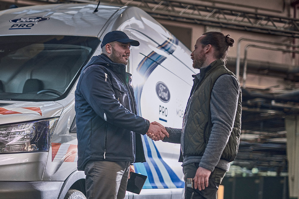 Twee mannen schudden elkaar de hand voor een Ford Mobile Service-bestelwagen in een werkplaats.