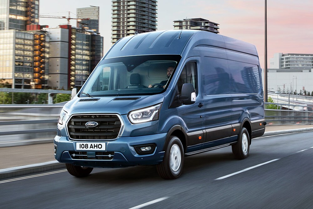 A Ford Transit driving across a bridge, a built-up urban cityscape in the background.