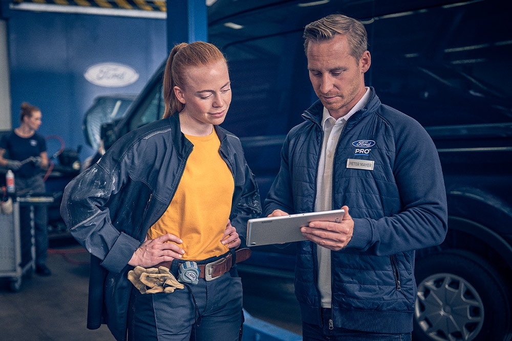 Ford-technicus en wagenparkbeheerder bekijken gegevens op een tablet in een garage.