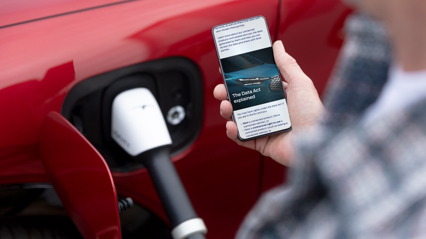 Een persoon leest uitleg over de Wetgeving inzake gegevensbescherming op zijn telefoon naast een elektrisch voertuig dat wordt opgeladen.