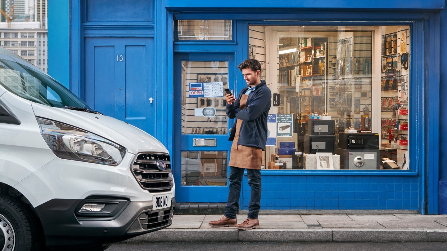 Person in front of shop checking his mobile with Ford Van parked next to shop