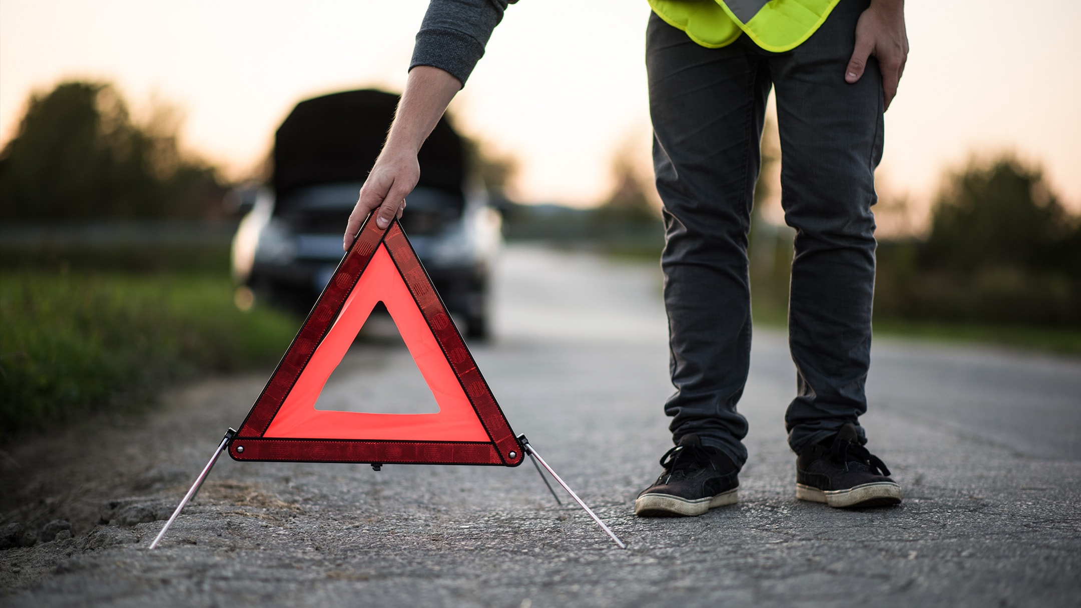 Een persoon plaatst een rode gevarendriehoek bij een auto die in panne is gevallen.