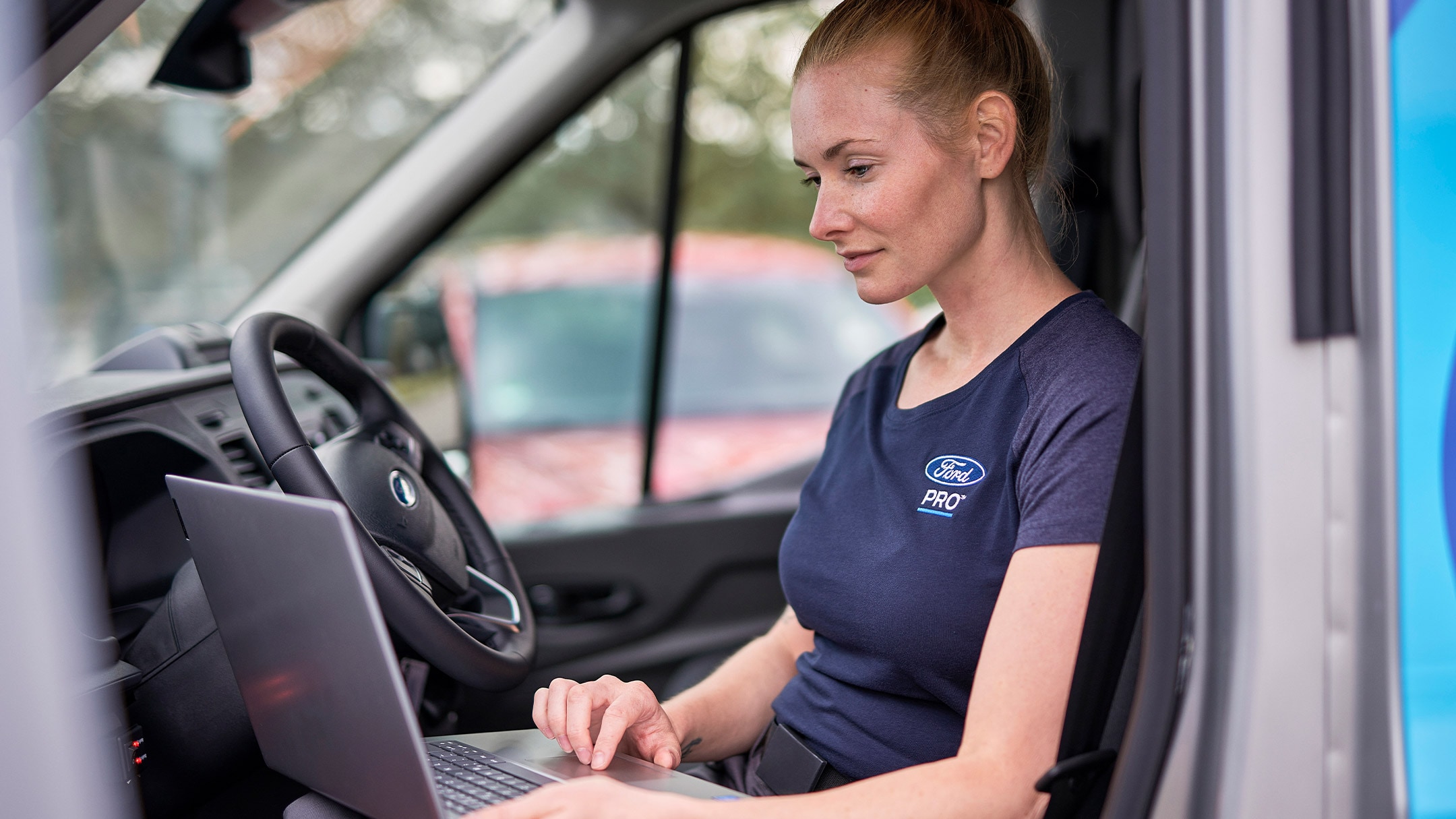 Een Ford Pro-expert zit in een auto en kijkt op een laptop tijdens een Ford-onderhoudsbeurt.
