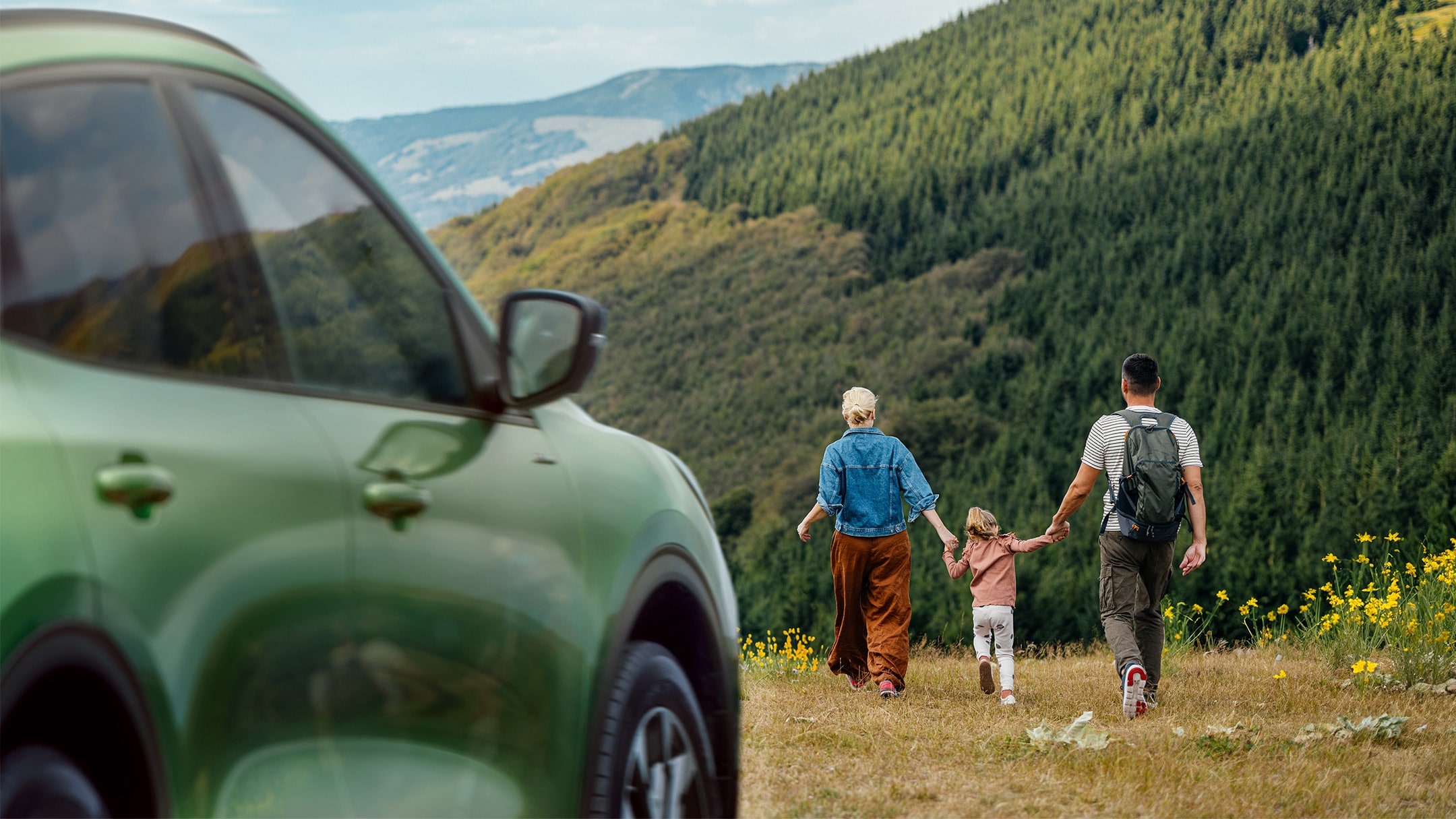 Gezin wandelt in een veld bij een groene Ford Kuga