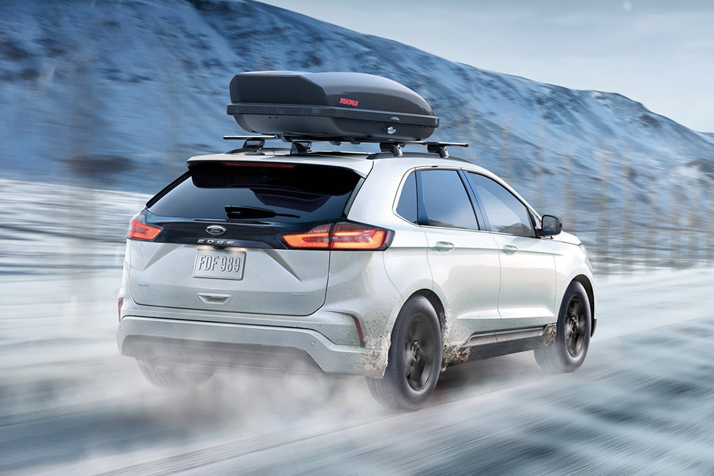 Witte Ford Edge met dakkoffer rijdt op besneeuwde bergweg, bewegingsonscherpte.