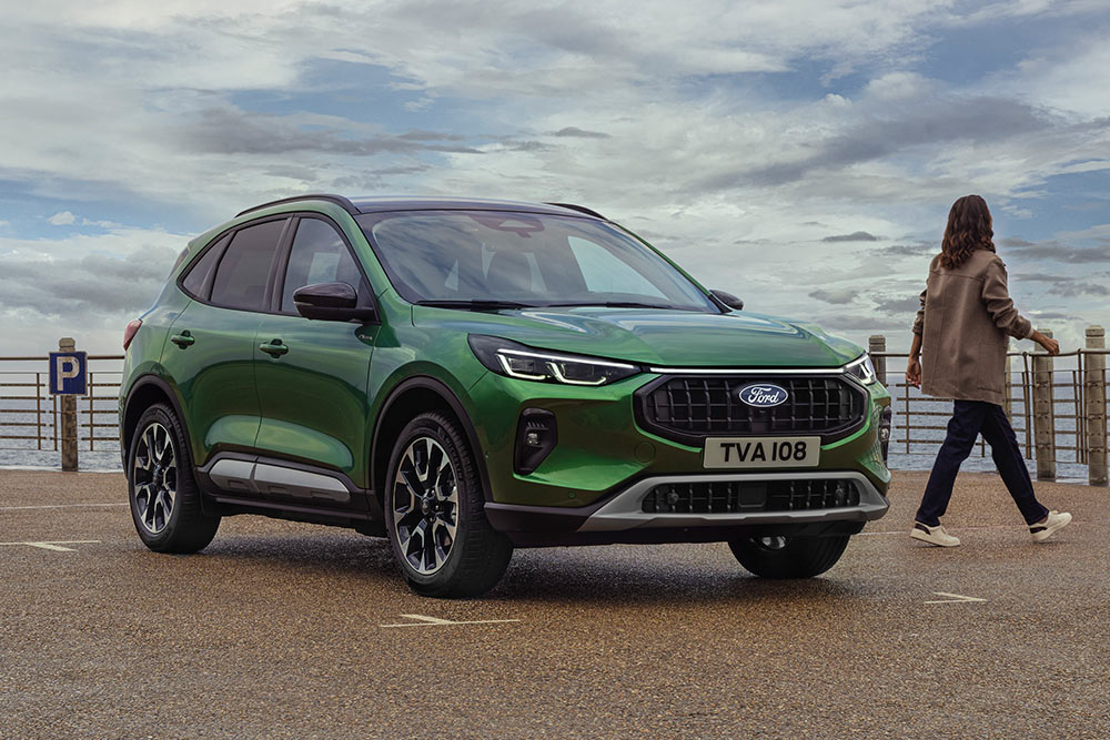  Vooraanzicht 3/4 van een groene Ford Kuga geparkeerd bij een kustreling, met twee personen in de buurt.