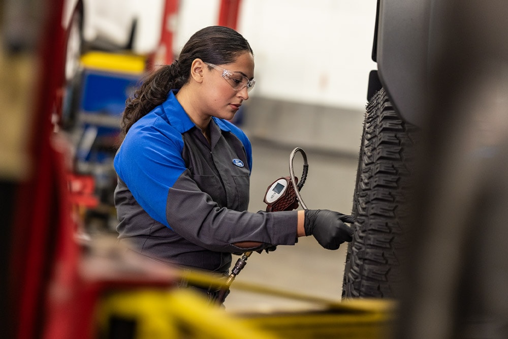 A Ford technician in safety glasses and gloves checks the tyre pressure of a vehicle. 