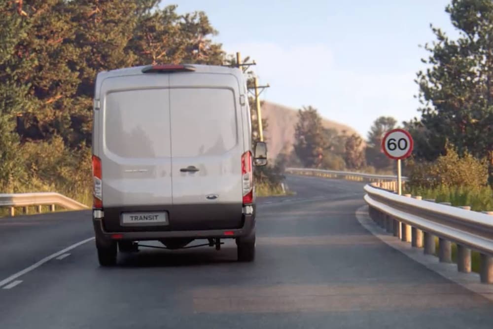 Een Ford Transit-busje rijdt over de weg, met een verkeersbord dat van achteren gezien wordt.